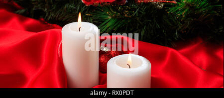 Décoration de Noël. Les bougies blanches sur la combustion de satin rouge sur un fond sombre, bannière, copy space Banque D'Images