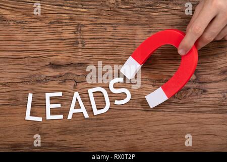 Person's Hand Holding Horseshoe aimant qui attire conduit blanc lettre sur fond de bois Banque D'Images