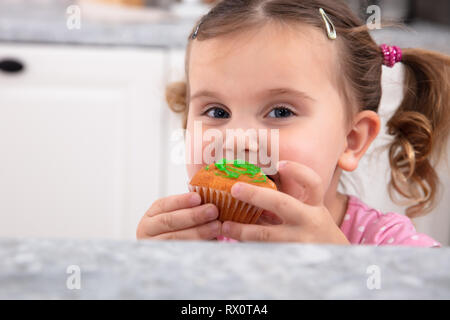 Portrait Of Happy Girl having fun while eating Cupcake savoureux dans la cuisine Banque D'Images