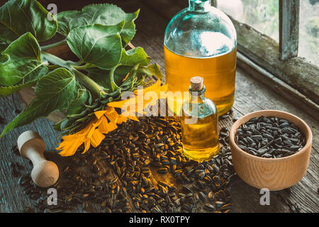 Bouteilles d'huile de tournesol, de mortier en bois et graines de tournesol jaune sur la table en bois à l'intérieur de la maison de village rétro. Banque D'Images