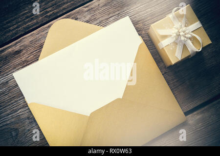 Enveloppe de papier jaune ouvert avec feuille de papier vierge et boîte-cadeau avec ruban sur planche de bois. Banque D'Images