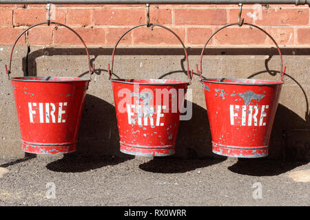 Trois rouges vieux seaux d'incendie vintage pendaison sur crochets à Maldon railway station, Victoria, Australie. Banque D'Images