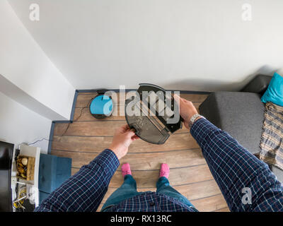 Homme tenant une poubelle remplie de déchets à un robot-aspirateur Banque D'Images
