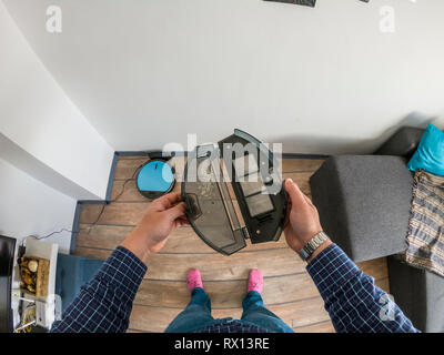 Homme tenant une poubelle remplie de déchets à un robot-aspirateur Banque D'Images