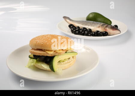 Burger de poisson avec de l'avocat et les olives, les tranches de fromage, assaisonné de sauce et salade verte pour un restaurant menu sur un fond isolé blanc Banque D'Images