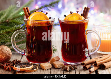 Tasses en verre de vin chaud avec des épices et des agrumes, des branches d'arbres de Noël et de feux arrière-plan flou sur. Banque D'Images