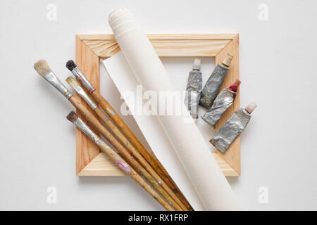 La barre de civière en bois, pinceaux, rouleau de toile d'artiste et de peinture tubes sur fond blanc de toile. Vue d'en haut. Banque D'Images