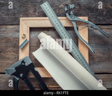 Rouleau de toile d'artiste, barre de civière civière toile, d'une pince, pistolet agrafeur et règle de mesure sur fond de bois. Vue d'en haut. Banque D'Images