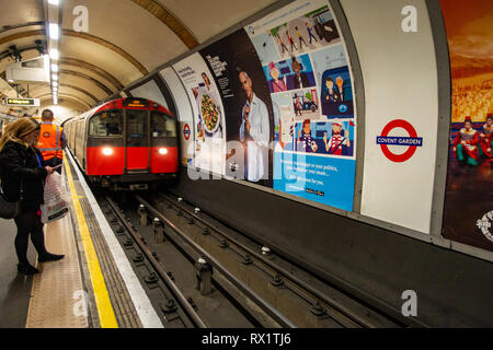 Banlieue femelle attend que l'approche de train de tube sur la voie du métro de Londres avec l'annonceur Banque D'Images