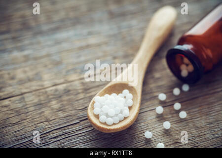 Cuillère en bois des globules homéopathiques, bouteille et granules épars. L'homéopathie médecine. Banque D'Images