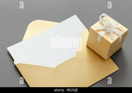 Enveloppe de papier jaune ouvert avec feuille de papier vierge et boîte-cadeau avec ruban sur fond gris. Banque D'Images