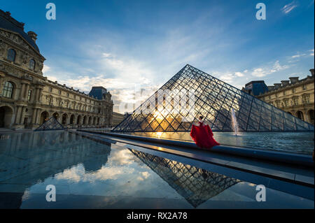 Modèle dans une robe rouge à la Pyramide du Louvre au coucher du soleil Banque D'Images