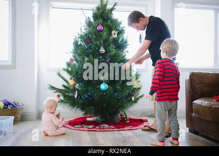 Père décorant l'arbre de noël tout en se tenant debout avec les enfants à la maison Banque D'Images