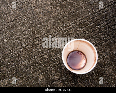 Taches de café dans le fond d'une tasse de papier à gauche sur le plancher de béton Banque D'Images