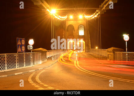 Feux arrière des voitures alors qu'ils se déplacent sur le Pont Suspendu de Menai à Anglesey, au nord du Pays de Galles de nuit. Banque D'Images