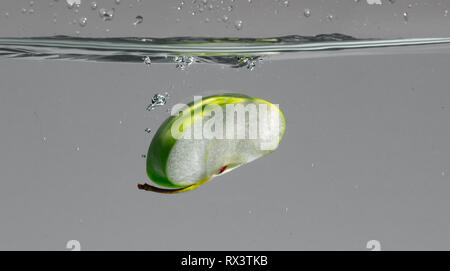 La tranche de pomme verte tombe dans l'eau et crée de belles bulles d'air et les projections d'eau Banque D'Images