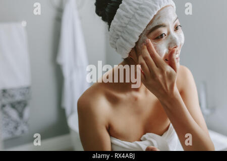 Jeune femme asiatique dans la salle de bains l'application de masque sur son visage. Femme à mettre masque sur son visage. Banque D'Images