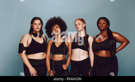 Portrait of young women standing ensemble contre l'arrière-plan gris. Groupe de femmes de différentes tailles, dans les vêtements de sport. Banque D'Images