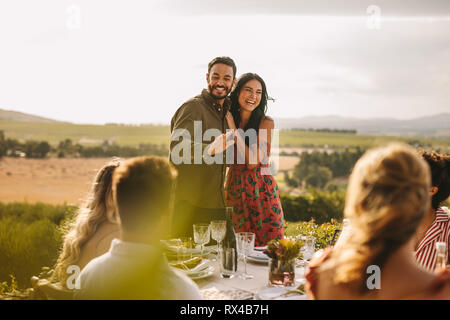 Couple amoureux lors d'une fête pour annoncer leur mariage à leurs amis. Sourit l'homme et de la femme de faire une annonce au cours d'un dîner à l'extérieur. Banque D'Images