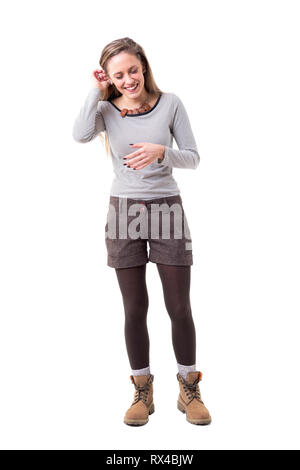 Jeune femme heureuse détendue franc rire et mettre de cheveux derrière l'oreille. Corps plein isolé sur fond blanc. Banque D'Images