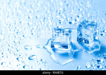 Deux cubes de glace fondue avec de l'eau tombe sur une table en verre Banque D'Images