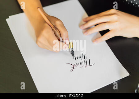 Calligraphe mains écrit une phrase sur du papier blanc. Expression - merci. L'inscription des lettres ornées d'ornement. La calligraphie, le graphisme, lettrage, Banque D'Images