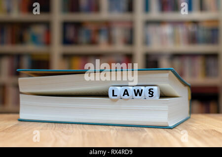 Dés dans un livre forment le mot 'loi'. Livre est couchée sur un bureau dans une bibliothèque. Banque D'Images