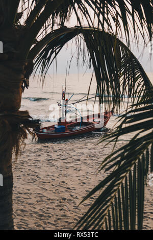 Longue queue thaï traditionnel bateau de pêche sous les palmiers sur la plage de Hua Hin au lever du soleil. Banque D'Images