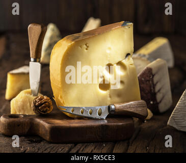 Morceau de fromage Maasdam du lait de vache sur planche de bois. Gamme de fromages à l'arrière-plan. Banque D'Images