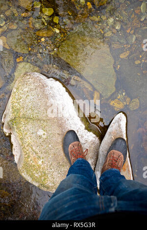 En regardant ses pieds avec des bottes de marche sur les rochers dans un petit ruisseau, tout en marchant dans les montagnes des Cévennes en France Banque D'Images