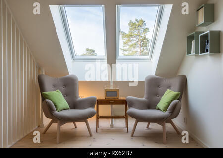 Design rétro moderne dans un grenier/loft. Petite table d'époque avec une radio et deux fauteuils de lecture dans deux puits de lumière. Banque D'Images