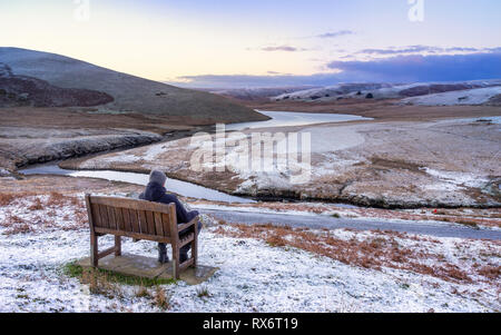 Pont AR, Elan Elan valley, le Pays de Galles. Scène enneigée d'Afon elan s'écoule autour de la montagne randonneur assis sur un banc, admirant la vue Banque D'Images