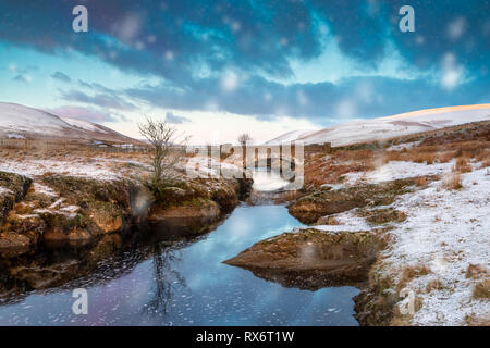 Pont AR, Elan Elan valley, le Pays de Galles. Scène enneigée d'Afon elan coule sous un pont avec un arbre isolé et Early sun Banque D'Images