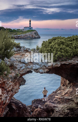 Porto Colom, à Majorque, archway naturel avec phare. Montres homme lever du soleil sur la Méditerranée Banque D'Images