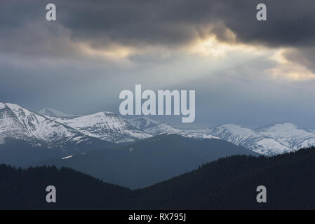 Paysage de printemps avec ciel d'orage. Dernière neige sur les sommets des montagnes. Un rayon de soleil depuis les nuages. Carpates, Ukraine Banque D'Images