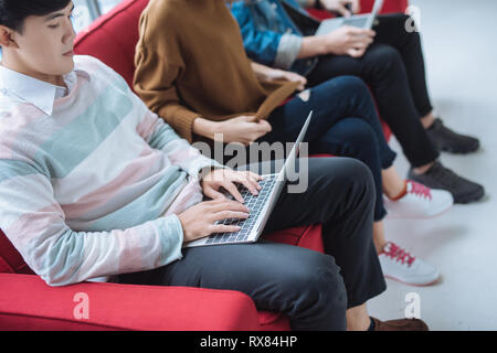 Groupe d'amis assis sur le canapé à l'aide de la technologie de l'ordinateur portable et smartphone Banque D'Images