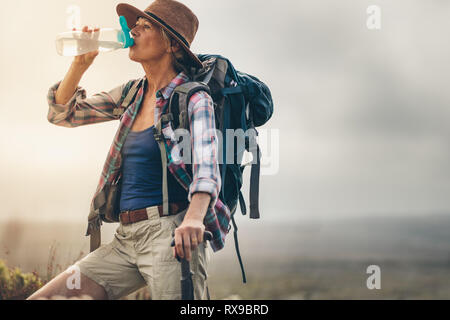 Close up of a senior female hiker prenant une pause au cours de son périple et de l'eau potable. Vue latérale d'une femme portant des chaussures de randonnée et sac à dos potable hat wate Banque D'Images