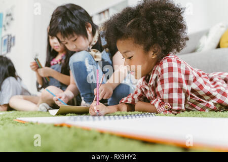 Groupe de petits enfants d'âge préscolaire du papier à dessin avec des crayons de couleurs . portrait de jeune fille africaine avec l'éducation amis concept. Banque D'Images