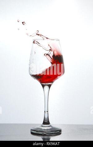 Close-up of red wine splashing in glass on table sur fond blanc Banque D'Images