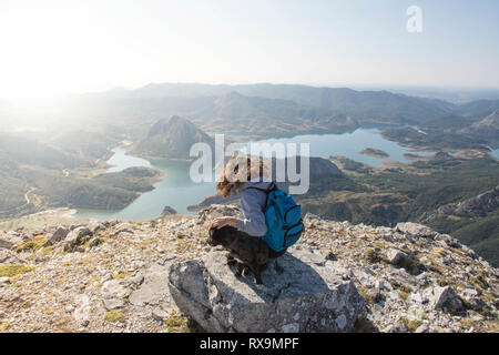 Vue arrière du female hiker avec chien assis sur la montagne contre un ciel clair au cours de journée ensoleillée Banque D'Images