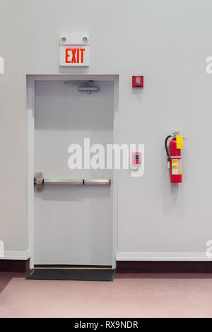 Shot verticale d'une porte de sortie de secours, d'alarme incendie avec un extincteur, et un éclairage de secours accroché au mur à côté de lui. Banque D'Images