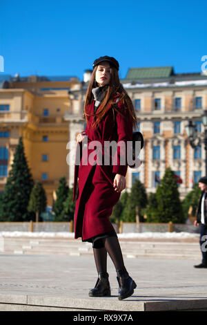 Portrait complet du corps. Belle jeune femme brune en élégant dans un long manteau bourgogne walking in spring street Banque D'Images