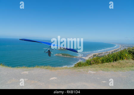 Le décollage des sauts pilote deltaplane motorisé avec pente de plages pittoresques de Mount Maunganui étend à horizon ci-dessous. Banque D'Images