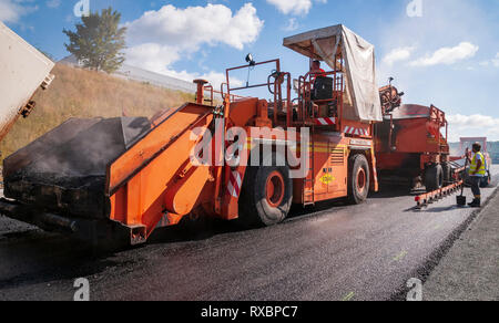 Train d'asphalte pour pavage. Au premier plan, le véhicule de transférer l'asphalte de ses wagons-trémies remplis par des camions pour le paver... Banque D'Images