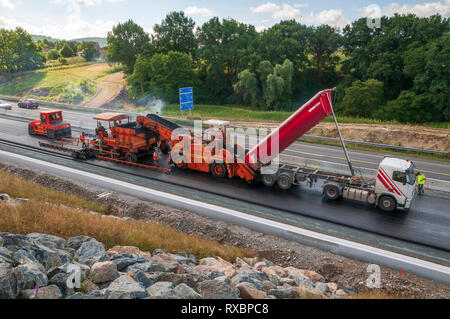 L'application d'asphalte sur une voie express. L'ensemble de l'équipement en action l'asphalte camion, véhicule de transfert, module de finition et compacteurs. Banque D'Images