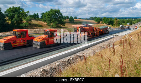 L'application d'asphalte sur une voie express. L'ensemble de l'équipement en action l'asphalte, camion, véhicule de transfert et de finition rouleau pneus compacteurs. Banque D'Images