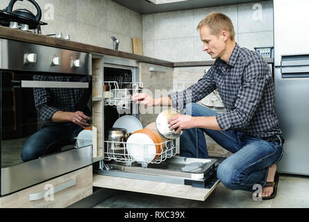 L'homme a poussé la vaisselle dans le lave-vaisselle. Banque D'Images