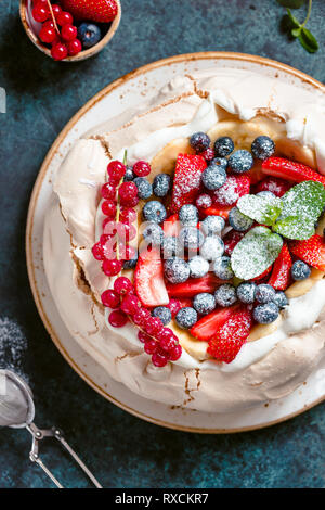 La NOUVELLE ZELANDE Pavlova gâteau avec la crème fouettée et mélange de baies fraîches sur un fond texturé bleu. Banque D'Images