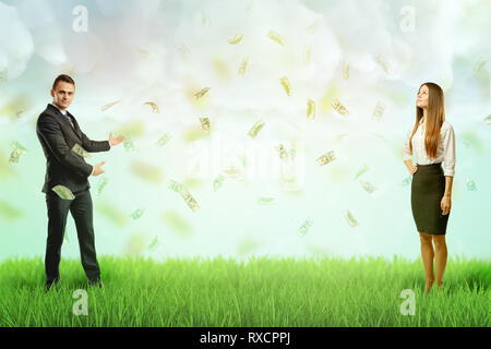 Businessman and businesswoman standing à chaque autre aspect de la pelouse verte et de pluie de dollars dans l'air. Banque D'Images