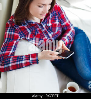 Young woman using mobile phone at home sitting on sofa relaxing Banque D'Images